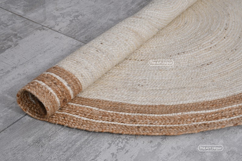 K&ouml;nnte beinhalten: Ein runder Naturfaser-Teppich mit einem wei&szlig;en Zentrum und einem braunen Jute-Rand. Der Teppich ist aufgerollt und zeigt die Textur der Jute.
