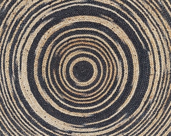 May include: Circular jute rug with a concentric design. Alternating bands of black and natural beige create a spiral pattern. The rug's texture is visible, showcasing the woven construction. This rug is suitable for indoor use.