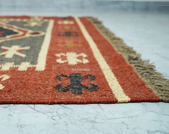 May include: A red, black, and cream colored rug with a geometric pattern. The rug has a fringe border and is made of natural fibers.