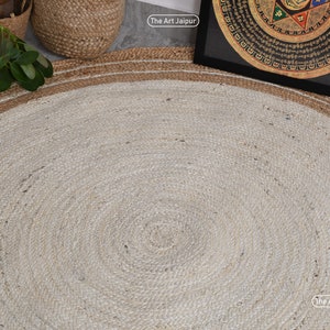 K&ouml;nnte beinhalten: Ein runder Jute-Teppich mit einem wei&szlig;en Zentrum und einem braunen Rand. Der Teppich hat eine nat&uuml;rliche, gewebte Textur. Der Text "The Art Jaipur" ist in der unteren rechten Ecke des Bildes sichtbar.