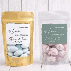 May include: Three candy bags with labels saying "all you need is Love and a little candy" and a name and date. The bags contain blue sweets, pink sweets, and assorted fruit sweets.
