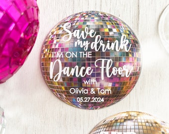 May include: A set of four round, silver disco ball drink markers with the text "Save my drink I'm on the dance floor" and the names Olivia & Tom and the date 05.27.2024.