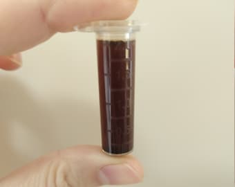 Puede incluir: Un cilindro graduado de plástico transparente con un líquido marrón en su interior. El nivel del líquido está a 1,5 ml.