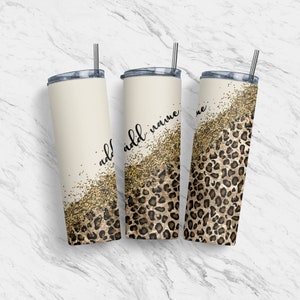 Pode incluir: Três copos de aço inoxidável com tampas e canudos. Os copos são decorados com um design de glitter dourado e estampa de leopardo. O copo do meio tem o texto "add name" escrito nele.