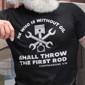 Può includere: Maglietta nera con una grafica bianca di chiavi incrociate e un pistone. Il testo recita "He who is without oil shall throw the first rod. Compressions 3:16."