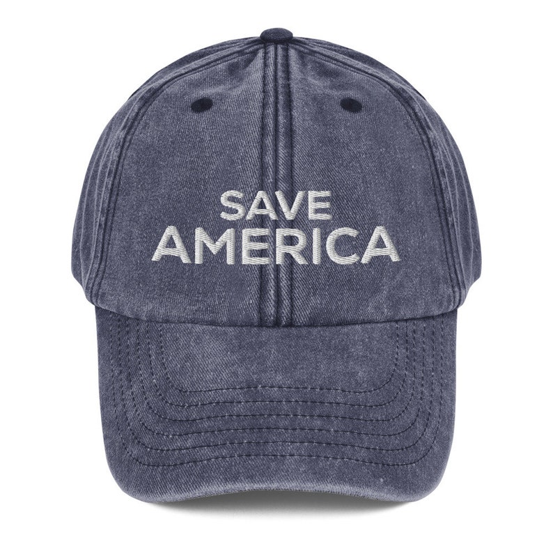Puede incluir: Una gorra de b&eacute;isbol de mezclilla azul con el texto "SAVE AMERICA" bordado en blanco en la parte delantera.