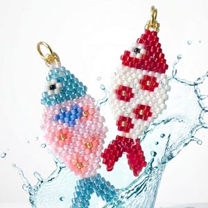 May include: Two fish-shaped charms crafted from small, colourful glass beads. One charm features light blue, pink, and gold beads, while the other displays red, white, and gold patterns. Each charm includes a gold-toned metal jump ring at the top.