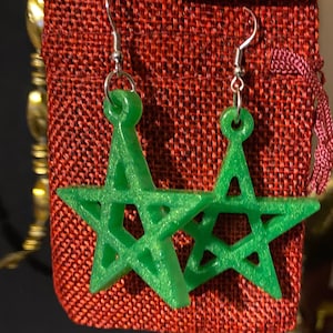 Puede incluir: Un par de pendientes de estrella verde con un gancho plateado. Los pendientes están hechos de un material brillante y tienen un diseño geométrico.