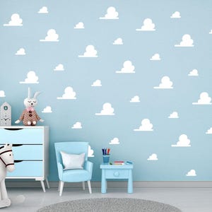 May include: A light blue wall adorned with white cloud decals. The room features a blue dresser, chair, and side table. A rocking horse and a stuffed bunny add to the playful atmosphere, ideal for a nursery.