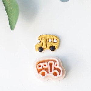 May include: A yellow school bus cookie cutter and a yellow school bus cookie. The cookie cutter is made of pink plastic and the cookie is made of yellow fondant.