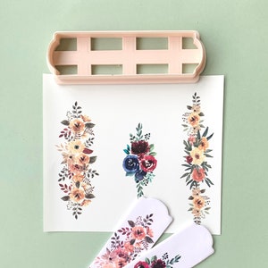 May include: A set of three floral cookie cutters, featuring a variety of flowers in shades of red, blue, yellow, and orange. The cutters are made of white plastic and have a scalloped edge.