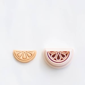 May include: Two plastic lemon slice cookie cutters, one in a light peach color and the other in a darker peach color. The cutters are stacked on top of each other.