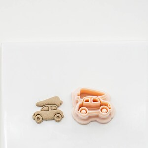 May include: A pink plastic cookie cutter shaped like a car with a Christmas tree on top, next to a brown cookie cut out in the same shape.