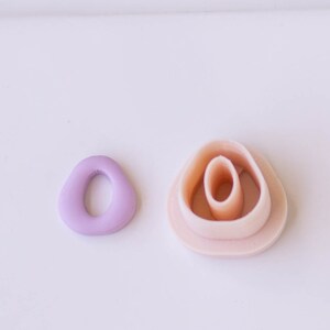 May include: Two pink and purple plastic cookie cutters shaped like a circle and a flower. The flower cutter has three layers.