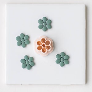 May include: Five green plastic flower-shaped cookie cutters, one of which is a larger pink cutter with a detailed design.