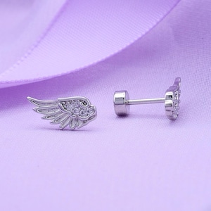 May include: A pair of silver-toned stud earrings shaped like angel wings, featuring small clear stones embedded along the wing feathers. The earrings include a straight post and a flat, circular screw-back closure for secure fastening.