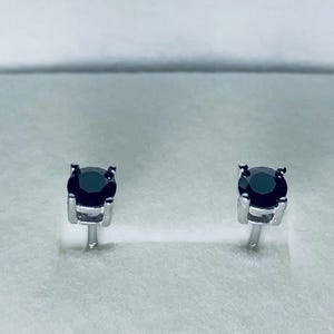 May include: A pair of stud earrings featuring round, black gemstones set in a silver metal. The earrings are displayed on a white surface, showcasing their simple yet elegant design. The gemstones appear to be approximately 0.25 inches in diameter.