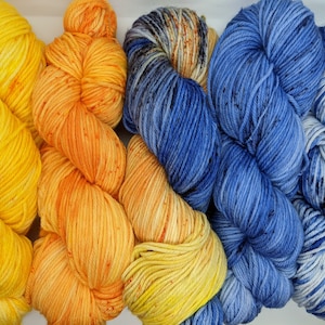 May include: A selection of colourful yarn skeins, featuring shades of yellow, orange, and blue. The yarn appears thick and hand-dyed, with vibrant colours. Ideal for knitting or crochet projects, the yarn is presented in a close-up shot.