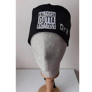 May include: Black scrub hat with white embroidery that reads "Straight Outta Plastic Surgery" and "Dr."