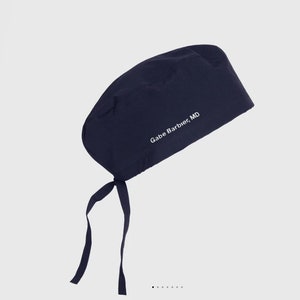 May include: Navy blue surgical scrub cap with tie-back closure. The cap features the text "Gabe Barbier, MD" in white. The cap is made of a soft, durable fabric.