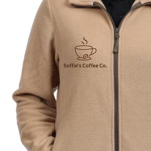 May include: A tan fleece jacket with a full-length zipper and a stand-up collar. The jacket features a brown logo of a coffee cup with steam and the text "Soffie's Coffee Co." on the chest.
