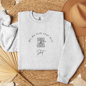 May include: A gray sweatshirt with the text "Hit me with your best shot" and a graphic of a coffee maker with a cup of coffee.