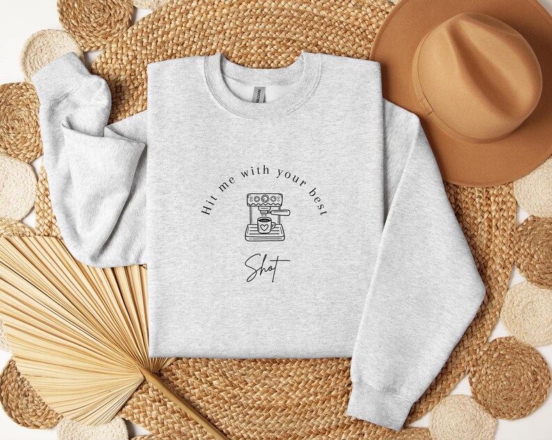 May include: A gray sweatshirt with the text "Hit me with your best shot" and a graphic of a coffee maker with a cup of coffee.