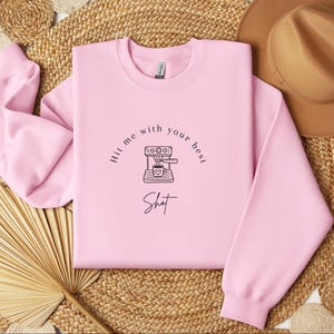 May include: Pink sweatshirt with a black and white illustration of a coffee maker and the text "Hit me with your best shot".