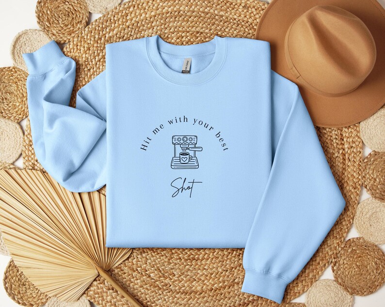 May include: A light blue sweatshirt with a graphic of a coffee maker and the text "Hit me with your best shot".