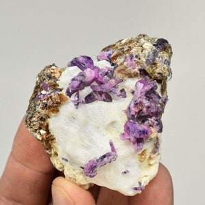 May include: A cluster of purple and pink corundum crystals on a white matrix. The crystals are sharp and well-formed, with a glassy luster. The matrix is covered in small, brown crystals.