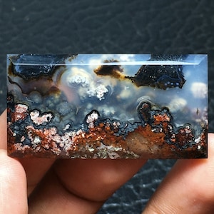 Op de afbeelding: Een gepolijste agaatplaat met een uniek patroon van wit, bruin en zwart. De agaat heeft een gelaagde uitstraling met verschillende texturen.