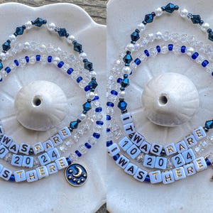 May include: Two layered necklaces with blue and white beads. The necklaces have white beads with black lettering that reads "It was rare 10 20 24 I was there". One necklace has a crescent moon charm and the other has a star charm.