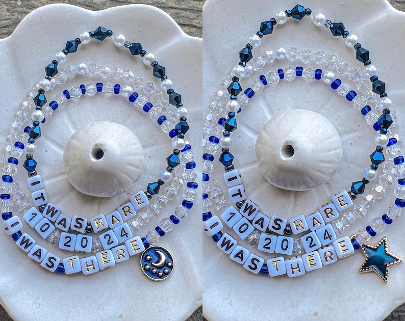 May include: Two layered necklaces with blue and white beads. The necklaces have white beads with black lettering that reads "It was rare 10 20 24 I was there". One necklace has a crescent moon charm and the other has a star charm.