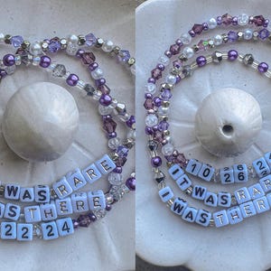 May include: A purple and white beaded necklace with a charm that says "It Was Rare I Was There" with the numbers 10, 26, 24, 11, 22, and 24.