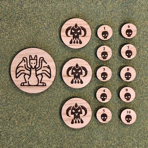 Pode incluir: Um conjunto de 10 fichas de madeira com ilustrações em preto e branco. As fichas representam um dragão, uma caveira com chifres e os números de 1 a 10.