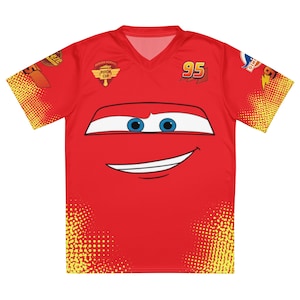Könnte beinhalten: Rotes V-Ausschnitt-T-Shirt mit einem lächelnden Cartoon-Autogesicht mit blauen Augen. Die Nummer 95 befindet sich oben rechts, und die Ärmel haben ein gelbes und rotes Punktmuster. Das Shirt trägt auch die Worte "Piston Cup".