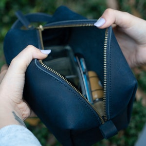 May include: A dark blue leather zippered pouch with a gold zipper. The pouch is open and has various items inside.