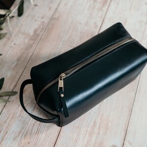 May include: A black leather travel toiletry bag with a gold zipper and a leather handle.