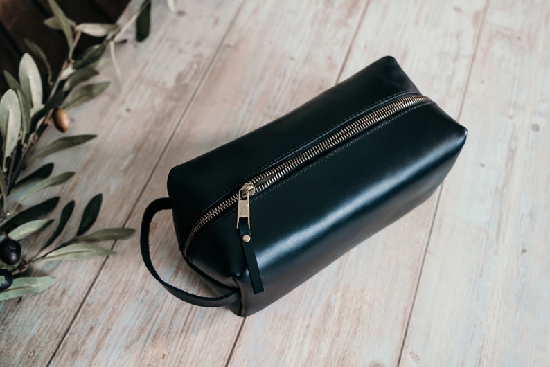 May include: A black leather travel toiletry bag with a gold zipper and a leather handle.