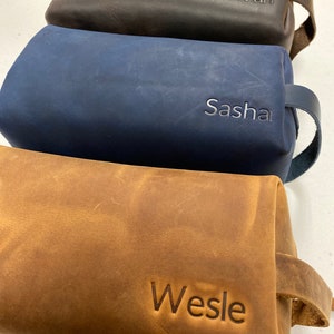 May include: Three leather toiletry bags with personalized names. The top bag is brown, the middle bag is blue, and the bottom bag is tan. The names are "Ivan", "Sasha", and "Wesle".