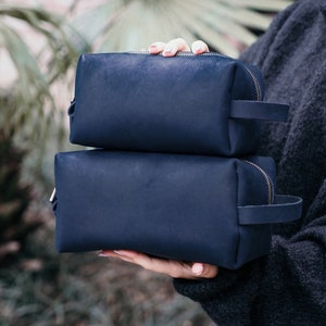 May include: Two navy blue leather travel toiletry bags with zipper closures and leather handles.