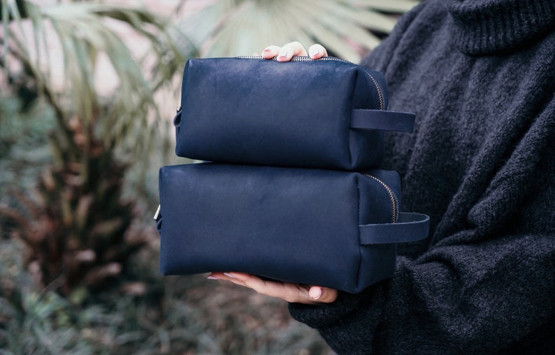 May include: Two navy blue leather travel toiletry bags with zipper closures and leather handles.