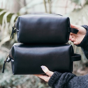 May include: Two black leather zippered travel pouches stacked on top of each other.