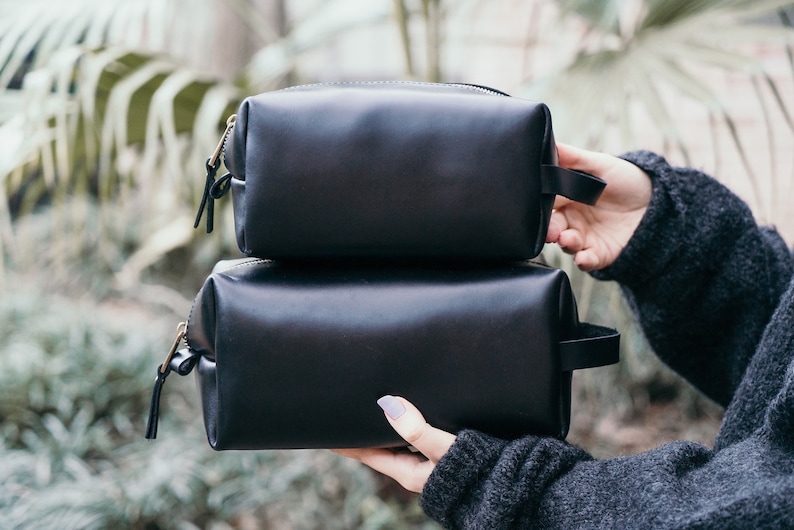 May include: Two black leather zippered travel pouches stacked on top of each other.