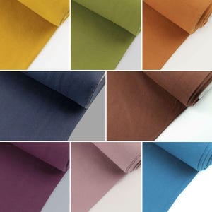 Könnte beinhalten: Eine Sammlung von Stoffproben in verschiedenen Farben, darunter Senfgelb, Olivgrün, gebranntes Orange, Marineblau, Burgunderrot, Altrosa und Tealblau. Der Stoff ist ein weiches, dehnbares Strickmaterial.