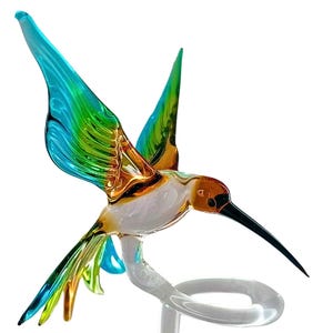 Könnte beinhalten: Eine Glasfigur eines Kolibris mit schillernden blauen, grünen und gelben Flügeln. Der Kolibri ist im Flug mit ausgestrecktem Schnabel und sitzt auf einem klaren Glasständer.