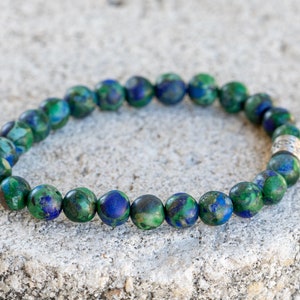 May include: A green and blue gemstone bracelet with a silver bead accent. The bracelet is made of round beads and is approximately 7 inches in length.