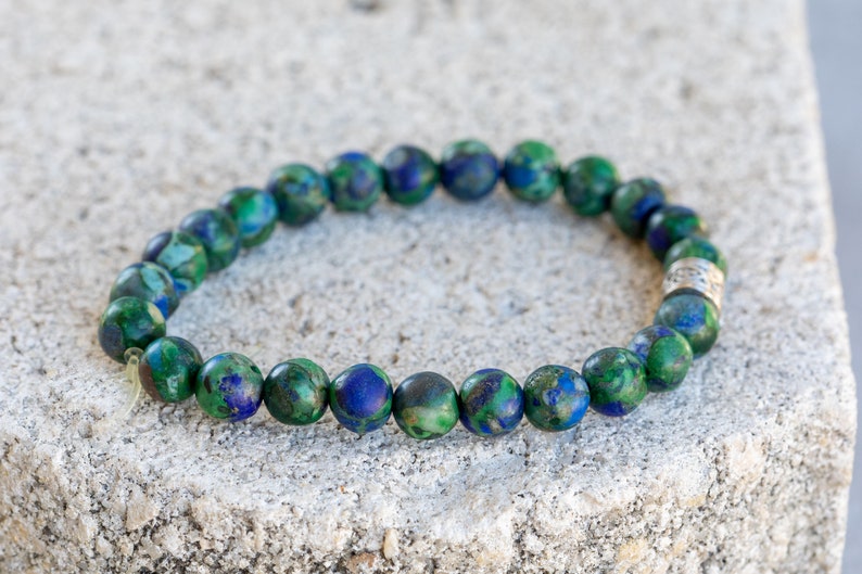 May include: A green and blue gemstone bracelet with a silver bead accent. The bracelet is made of round beads and is approximately 7 inches in length.