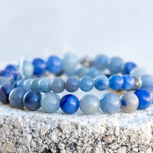 May include: Two bracelets made of blue gemstone beads. The beads are different shades of blue, ranging from light to dark.
