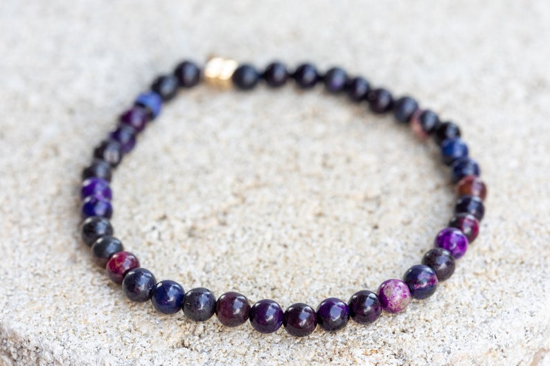 May include: A purple, blue, and black beaded bracelet with a gold clasp.